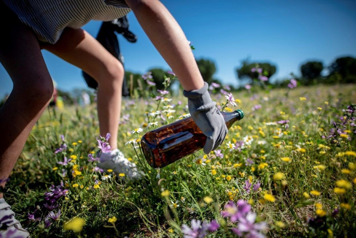 Joven recogiendo una botella de vidrio en el campo ECOEMBES