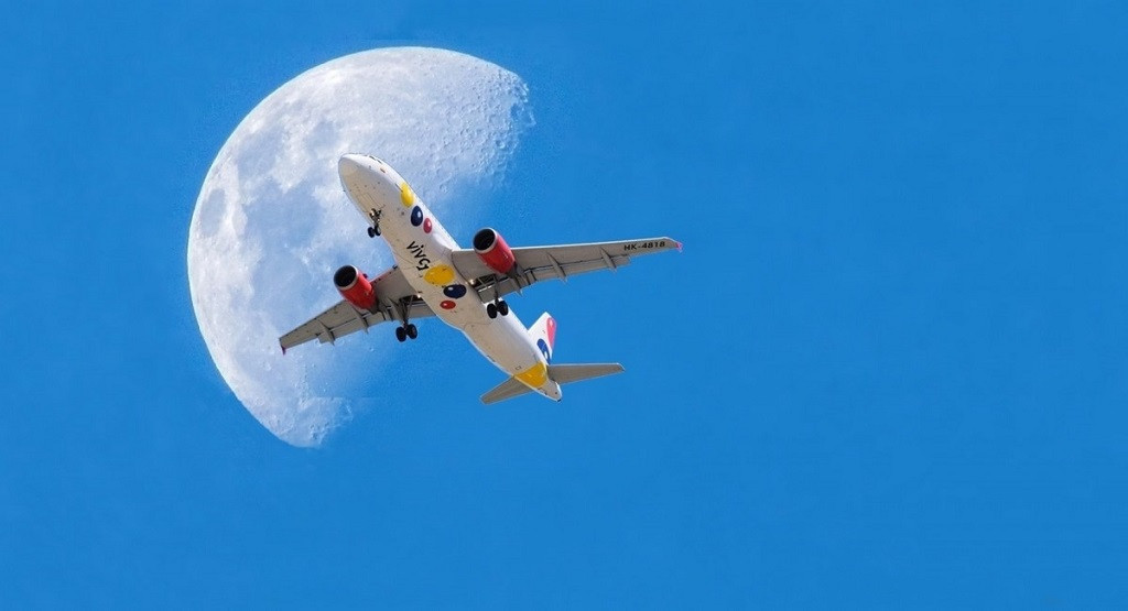 Aviu00f3n pasando frente a la Luna sobre un cielo azul