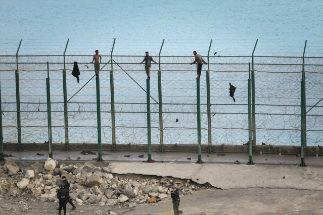 En la image, tres de un total de 153 migrantes, entran en Ceuta saltando su doble valla en la primera incursión en grupo en un año.