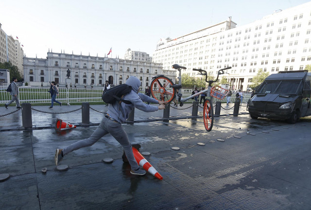18 October 2019, Chile, Santiago: A man throws a bike during a protest against the rising costs for subway and bus tickets. Photo: Cristobal Escobar/Agencia Uno/dpa