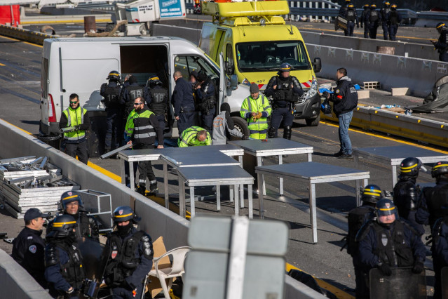 Varios operarios desmontan las mesas colocadas por los manifestantes en la carretera de la N-II durante su corte, rodeados por agentes de la policía francesa, en La Jonquera
