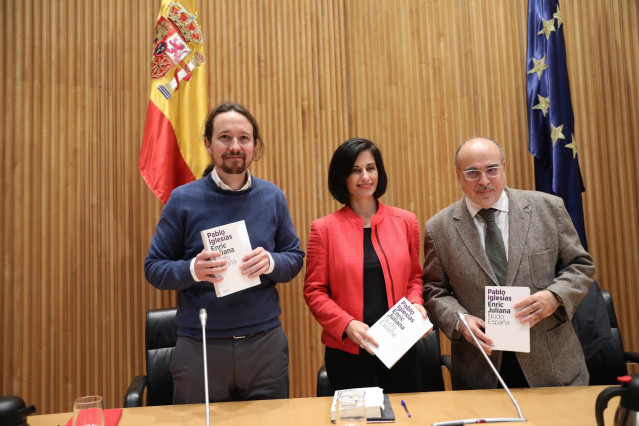 (I-D) El secretario general de Podemos, Pablo Iglesias; la periodista Lola García como moderadora y el periodista Enric Juliana posan con el libro del evento durante el diálogo `Nudo España: un año después´ en el Congreso de los Diputados