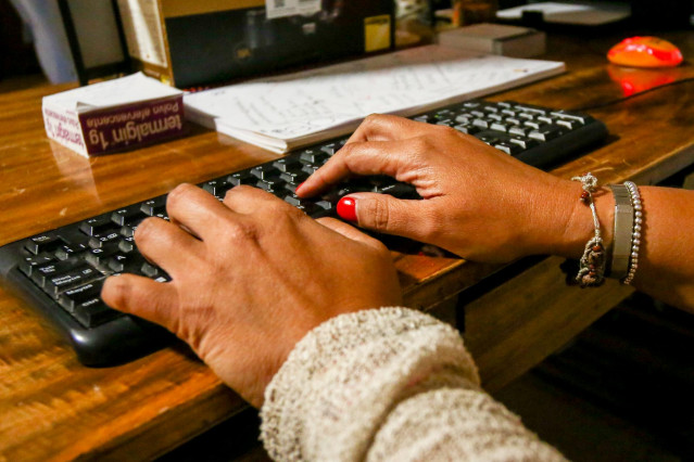 Unas manos de mujer escriben en el teclado de un ordenador, sobre una mesa de madera.