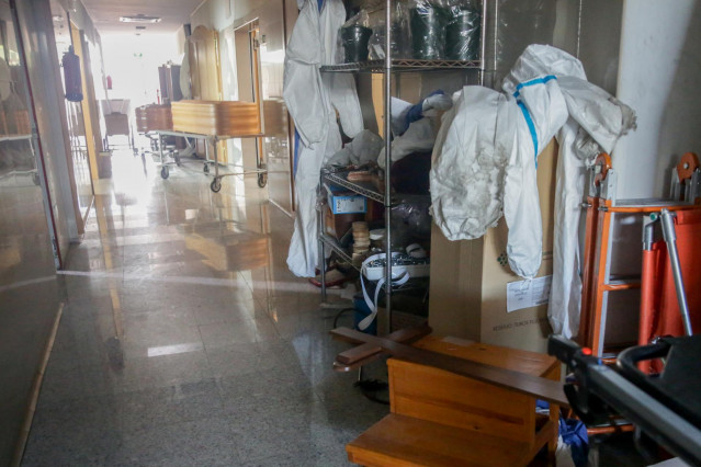 Varios ataúdes y varios trajes de protección en un pasillo del Tanatorio Crematorio Mémora Coslada