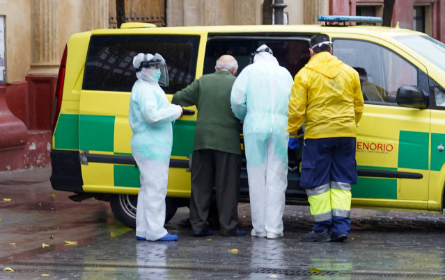Sanitarios de la residencia de San Juan de Dios, ataviados con EPIs, acompañan a un anciano hacia la ambulancia que lo llevará al hospital Virgen del Rocío de Sevilla.