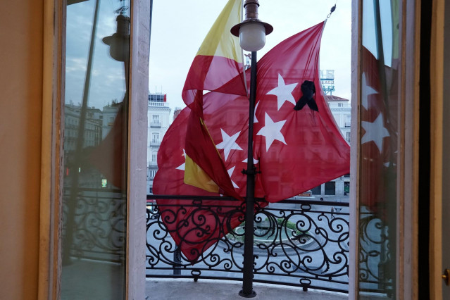 Vista desde el interior de las dependencias de la sede de la Comunidad de Madrid en la Puerta del Sol, con las banderas a media asta y un crespón negro en la bandera regional por los fallecidos por coronavirus, después de que la Comunidad de Madrid haya c