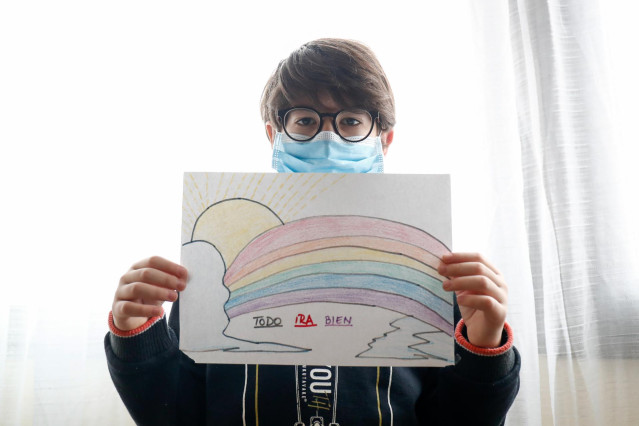 Un niño con mascarilla enseña un dibujo que ha hecho de un arcoiris y la frase 'Todo irá bien' cuando queda tan solo una semana para que niños y preadolescentes puedan salir a la calle durante el confinamiento por el coronavirus