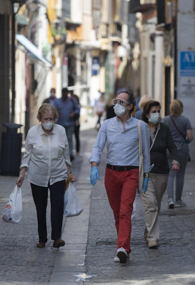 Varias personas caminan protegidas con mascarillas por una calle del centro de la ciudad, tras el nuevo acuerdo de Gobierno en el cual el uso de mascarillas será obligatorio también en la vía pública y en espacios cerrados cuando no se pueda garantizar el