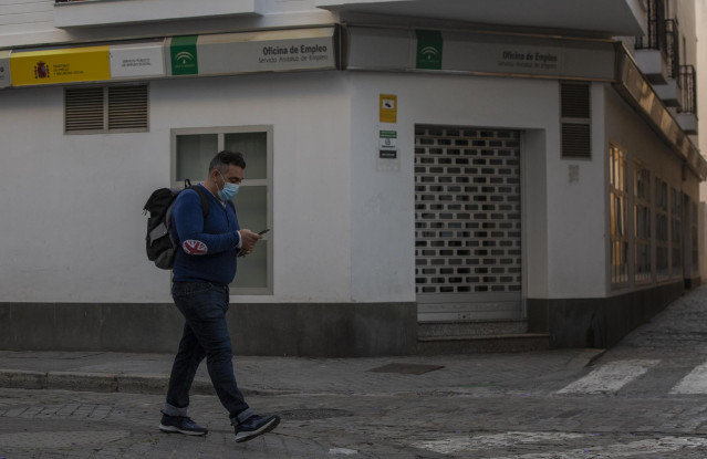 Un hombre protegido con mascarilla camina delante de una Oficina de Empleo
