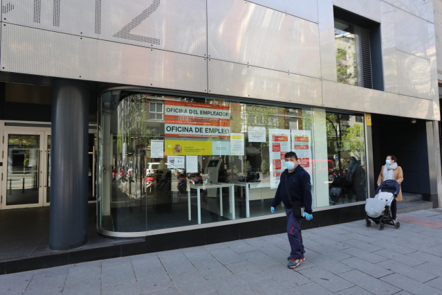 Un hombre con mascarilla y una mujer con un carrito de bebé pasan frente a una oficina de Empleo
