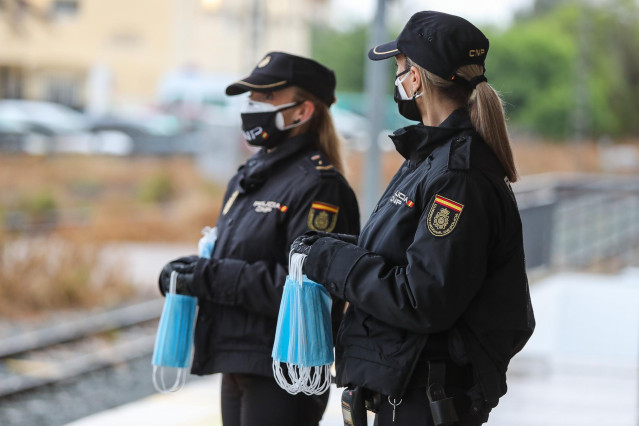Policías nacionales se preparan para entregar mascarillas a los viajeros que esperan en un andén durante el estado de alarma