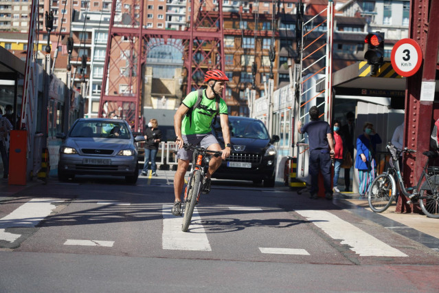 Un ciclista y dos coches cruzan el Puente de Vizcaya, también conocido como Puente Bizkaia que une las dos márgenes de la ría de Bilbao en Bizkaia