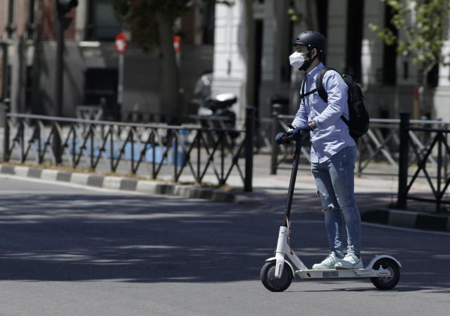 Un hombre protegido con mascarilla monta en un patinete eléctrico durante el primer día del uso obligatorio de mascarilla, impuesto por el Gobierno, en la vía pública, en espacios al aire libre y en cualquier espacio cerrado de uso público o que se encuen