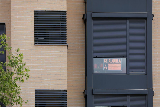 En la fachada de un edificio se ve un cartel de 'Se Alquila' bajo la persiana de uno de los pisos.