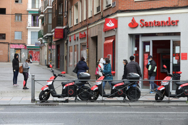 Varias personas esperan para entrar a una oficina del Banco Santander.