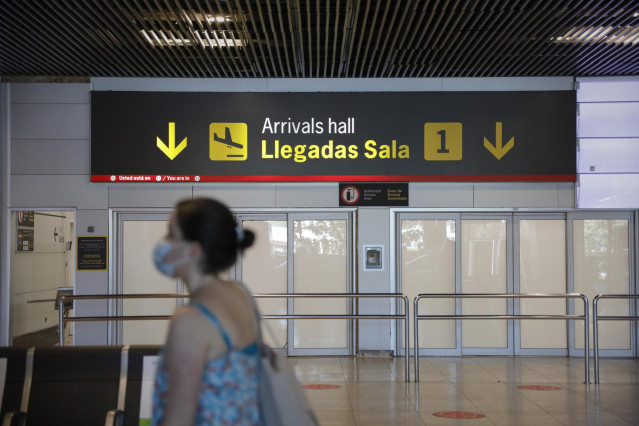 Una persona con mascarilla pasa junto a la entrada de la sala de llegadas 1 de la Terminal 1 del Aeropuerto de Barajas, en Madrid (España).