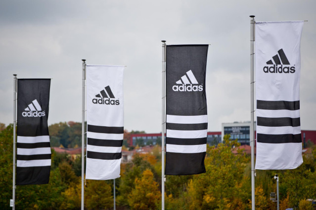 FILED - 15 October 2013, Bavaria, Herzogenaurach: Flags with the logos of the sporting goods manufacturer Adidas wave. Adidas' executive board member for global human resources, Karen Parkin, has stepped down after being accused of racism. Photo: Daniel K