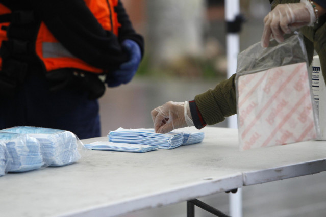 Transeúntes recogen mascarillas puestas a disposición de viajeros y usuarios de transporte público, en Palma de Mallorca, Islas Baleares, (España), a 14 de abril de 2020.