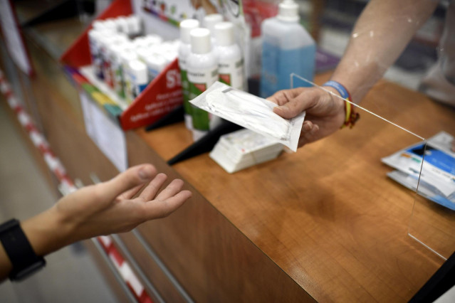 Un farmacéutico entrega a un cliente una de las mascarillas KN95 que ha recibido en su farmacia