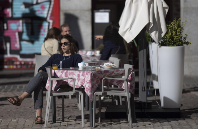 Una mujer disfruta en una terraza de la Plaza Mayor durante el primer día con nuevas restricciones en la movilidad.