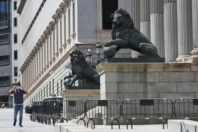 Un hombre se coloca una mascarilla mientras camina por delante de la fachada del Congreso