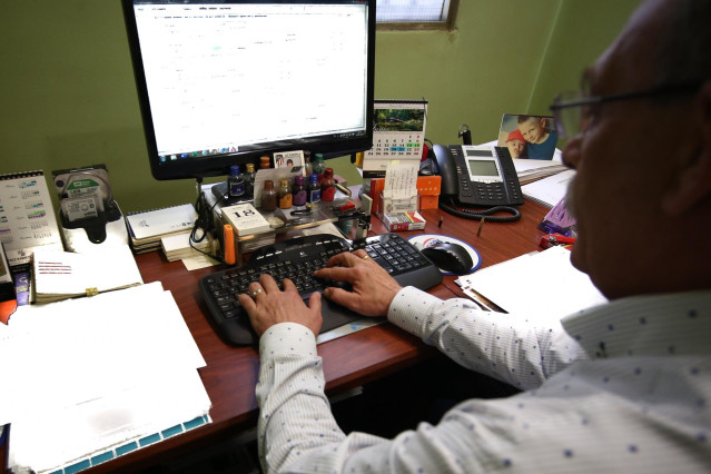 Un hombre escribe con el teclado de su ordenador, mientras trabaja en el despacho de su oficina.