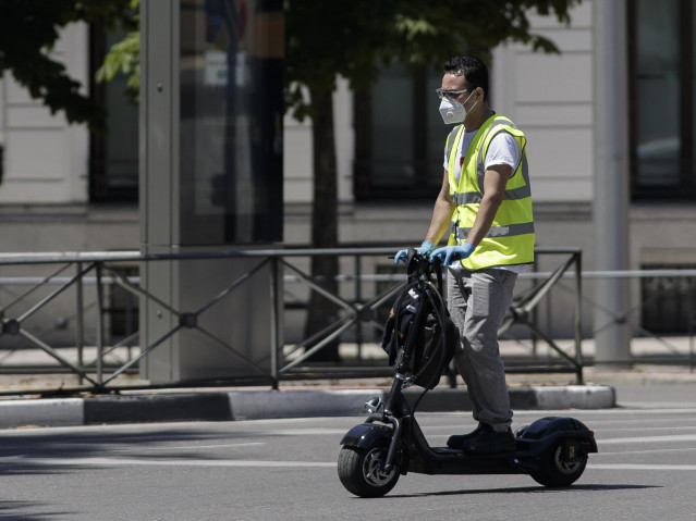 Un hombre protegido con mascarilla monta en un patinete eléctrico durante el primer día del uso obligatorio de mascarilla, impuesto por el Gobierno, en la vía pública, en espacios al aire libre y en cualquier espacio cerrado de uso público o que se encuen