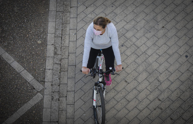 Una mujer en bicicleta haciendo uso de la mascarilla.