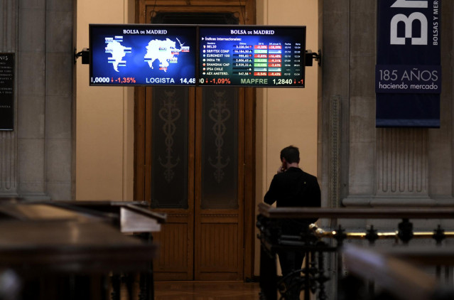 Una persona camina bajo los televisores indicativos con los valores del Ibex en el Palacio de la Bolsa de Madrid (España), a 2 de octubre de 2020.
