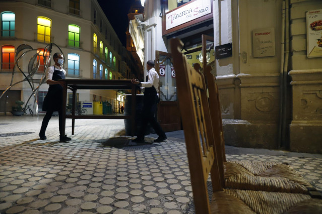 Dos camareros se afanan en recogen la terraza del bar ubicado en el centro de la capital, como  consecuencia del toque de queda impuesto por el Gobierno para poder frenar el contagio en Málaga a 27 de octubre 2020