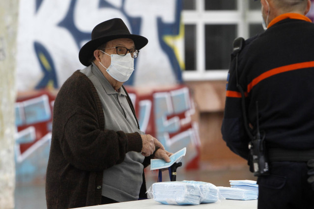 Transeúntes recogen mascarillas puestas a disposición de viajeros y usuarios de transporte público en las inmediaciones de la estación Intermodal en abril.
