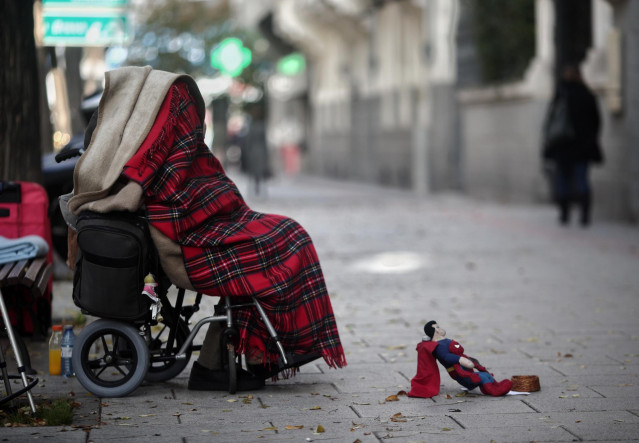 Una persona en silla de ruedas y tapada con una manta pide dinero en una calle de Madrid