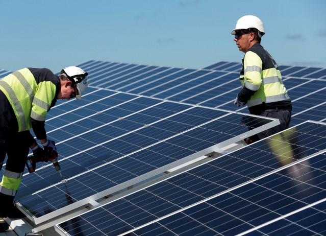 Dos operarios fijan paneles solares en la instalación.
