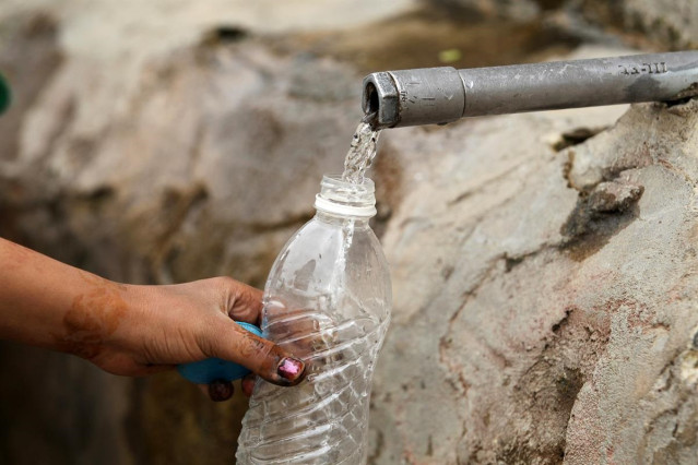 Mujer llenando una botella de agua en un grifo en la calle