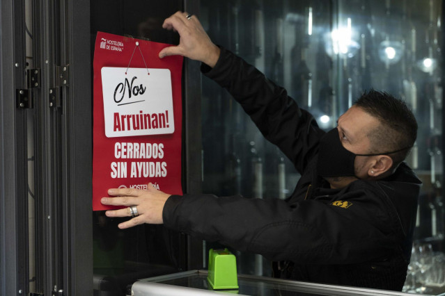 Un trabajador de hostelería coloca un cartel donde se lee 