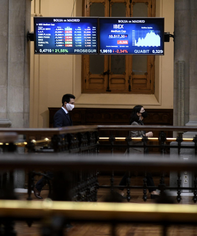 Dos personas caminan bajo los televisores indicativos con los valores del Ibex en el Palacio de la Bolsa de Madrid (España), a 2 de octubre de 2020.
