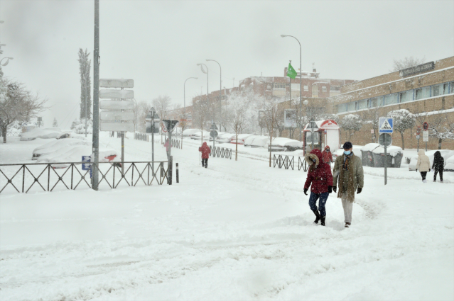 Algunas personas caminan por una calzada completamente cubierta de nieve de una calle en Alcobendas, Madrid.