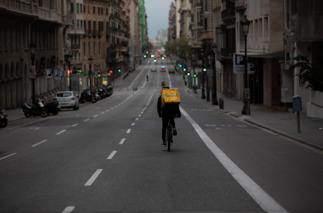 Un trabajador de Glovo en bicicleta por una calle de Barcelona, prácticamente vacía durante el primer día laborable de la segunda semana desde que se decretó el estado de alarma en el país a consecuencia del coronavirus, en Barcelona/Catalunya (España) a