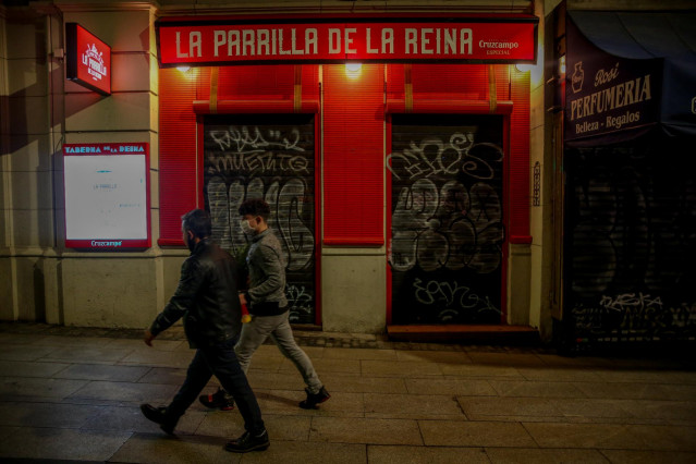 Dos jóvenes pasan por delante de un restaurante cerrado