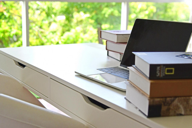 Archivo - Un escritorio con un ordenador portátil y varios libros.