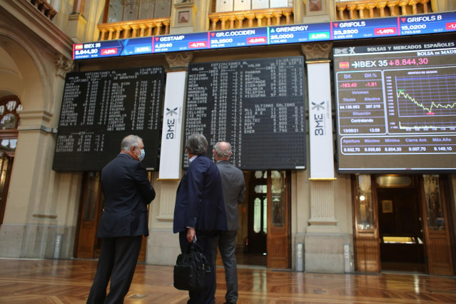 Tres hombres observan valores económicos en el Palacio de la Bolsa, a 13 de mayo de 2021, en Madrid (España). El Ibex 35 cedía un 1,94% en la media sesión de este jueves, alejándose de los 8.900 puntos, arrastrado por las caídas registradas ayer en Wall S