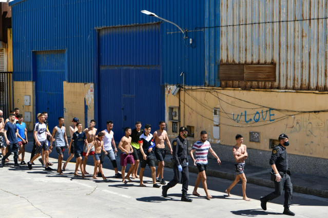 Un grupo de jóvenes migrantes marroquíes en fila en las inmediaciones de una nave de Ceuta tras acceder a la ciudad española