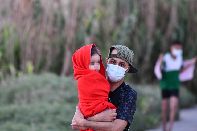 Un hombre migrante coge en brazos a una niña en la playa del Tarajal, a 17 de mayo de 2021, en Ceuta, (España). Más de 3.000 ciudadanos marroquíes, según las fuentes consultadas por Europa Press, han accedido irregularmente a Ceuta durante este lunes bord