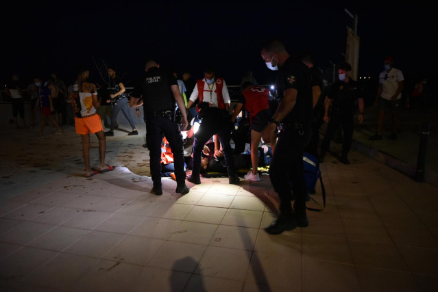 Agentes y empleados de Cruz Roja ayudan a grupos de migrantes tras su llegada a la playa del Tarajal.