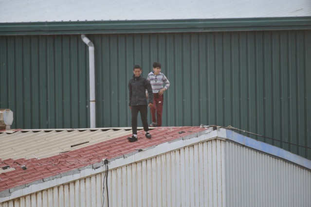 Dos niños caminan por un tejado al tratar de escapar de la nave de primera acogida del polígono del Tarajal, en Ceuta, en una imagen del pasado 20 de mayo