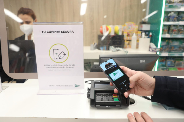Archivo - Una persona paga con el móvil en un centro comercial