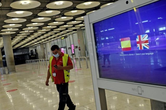 Archivo - Un operario de Iberia pasa al lado de un monitor con las banderas de España y Reino Unido en la T1 del Aeropuerto de Madrid-Barajas Adolfo Suárez, en Madrid (España), a 27 de julio de 2020.