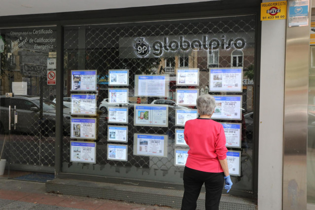 Archivo - Una mujer echa un vistazo a las ofertas de una agencia inmobiliaria