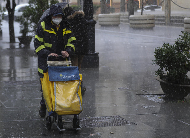 Archivo - Un repartidor de correos trabaja bajo la lluvia protegido con un impermeable.