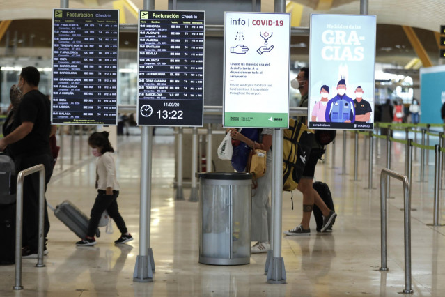 Archivo - Pasajeros cerca de páneles informativos en la terminal T4 del aeropuerto Adolfo Suárez Madrid-Barajas.